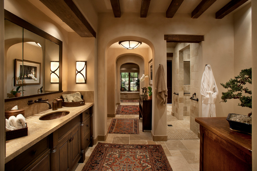 Inspiration for a large mediterranean master stone tile and beige tile limestone floor alcove shower remodel in Phoenix with an undermount sink, raised-panel cabinets, dark wood cabinets, limestone countertops and beige walls