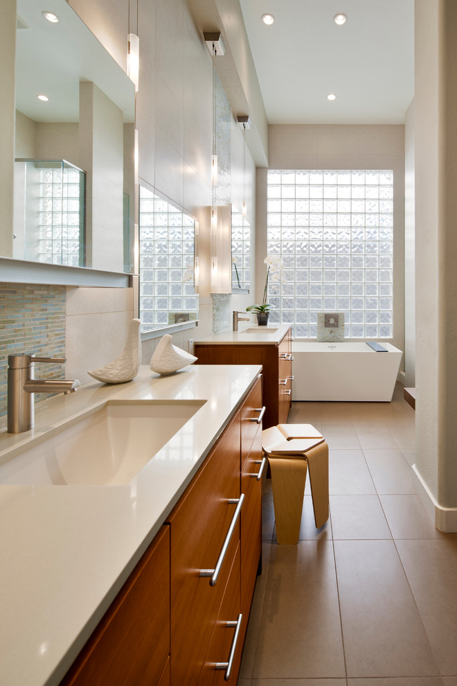 Modelo de cuarto de baño principal y rectangular, actual, de tamaño medio, con encimera de cuarzo compacto, bañera exenta, baldosas y/o azulejos de porcelana, lavabo bajoencimera, armarios con paneles lisos, puertas de armario de madera oscura, paredes beige, suelo de baldosas de porcelana, suelo beige y encimeras beige