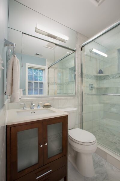 Inredning av ett klassiskt litet en-suite badrum, med ett undermonterad handfat, luckor med glaspanel, skåp i mörkt trä, marmorbänkskiva, en dusch i en alkov, en toalettstol med hel cisternkåpa, vit kakel, stenkakel, vita väggar och marmorgolv