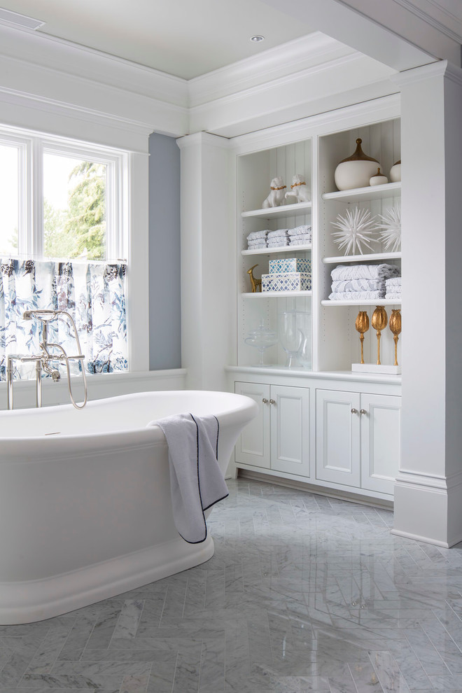 Klassisk inredning av ett stort en-suite badrum, med öppna hyllor, vita skåp, ett fristående badkar, marmorgolv, en toalettstol med separat cisternkåpa, grå väggar, ett undermonterad handfat, marmorbänkskiva och vitt golv