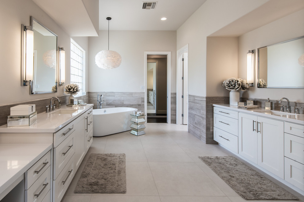 Aménagement d'une salle de bain classique avec un placard avec porte à panneau encastré, des portes de placard blanches, une baignoire indépendante, un mur gris, un lavabo encastré, un sol gris et un plan de toilette blanc.