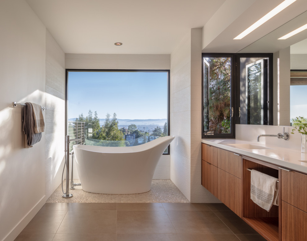Modernes Badezimmer mit flächenbündigen Schrankfronten, hellbraunen Holzschränken, freistehender Badewanne, weißen Fliesen, weißer Wandfarbe, integriertem Waschbecken, Quarzwerkstein-Waschtisch, weißer Waschtischplatte und grauem Boden in San Francisco