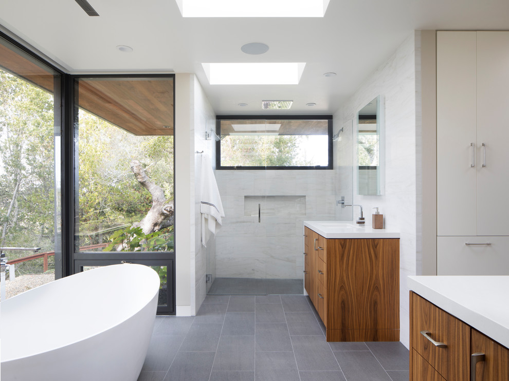 Design ideas for a large modern ensuite bathroom in San Francisco with flat-panel cabinets, medium wood cabinets, a freestanding bath, a walk-in shower, grey tiles, stone tiles, porcelain flooring, a submerged sink, engineered stone worktops, grey floors and an open shower.