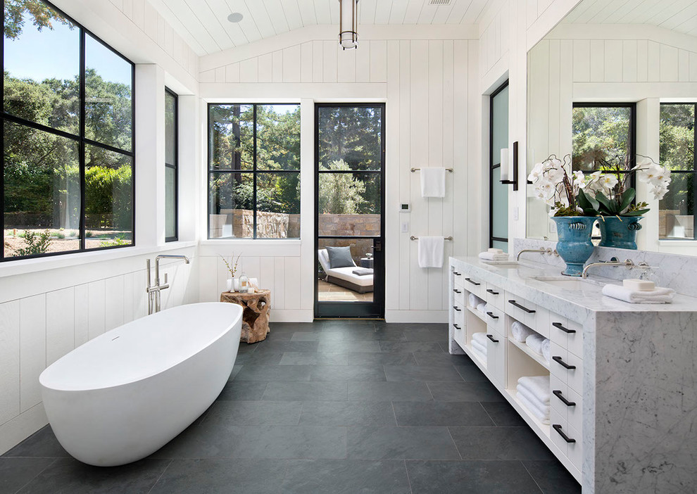 Inredning av ett lantligt en-suite badrum, med öppna hyllor, vita skåp, ett fristående badkar, vita väggar, ett undermonterad handfat, grått golv, skiffergolv och marmorbänkskiva