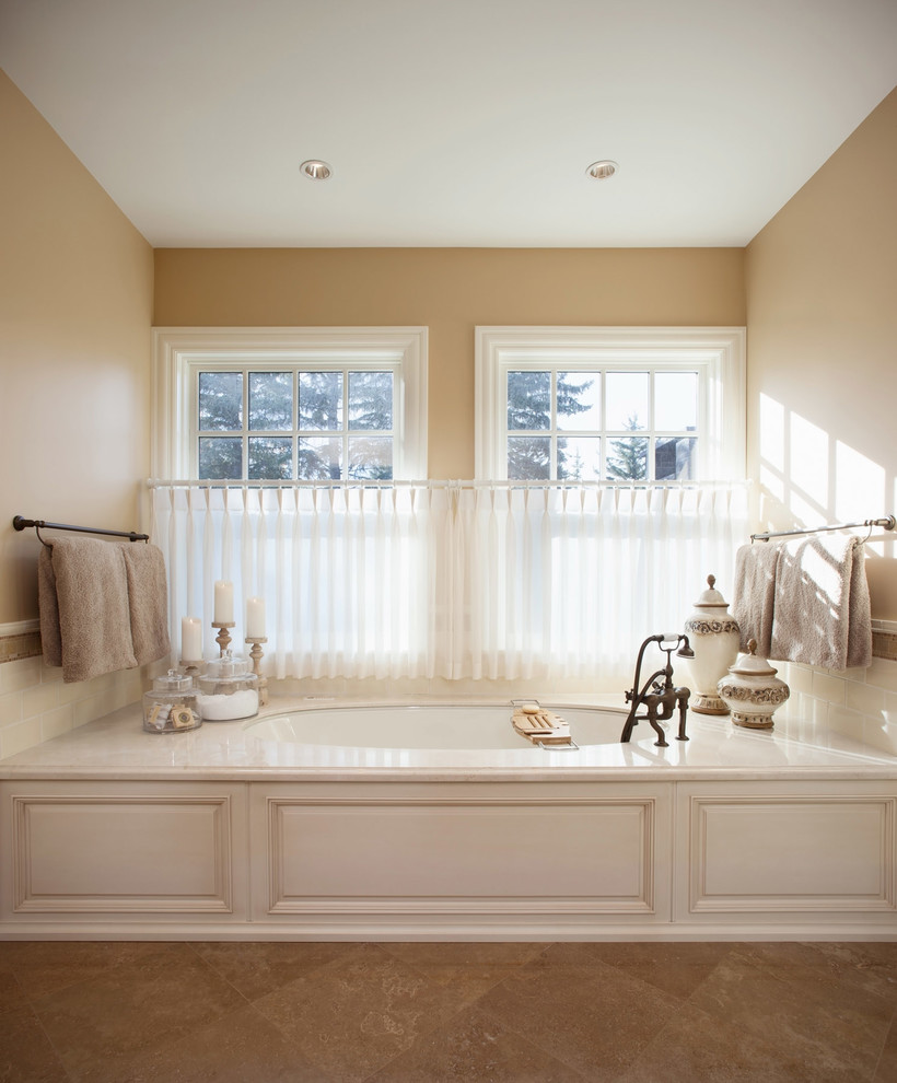 Стильный дизайн: огромная главная ванная комната в классическом стиле с фасадами с выступающей филенкой, белыми фасадами, мраморной столешницей, полновстраиваемой ванной, бежевой плиткой, керамической плиткой, бежевыми стенами и полом из известняка - последний тренд