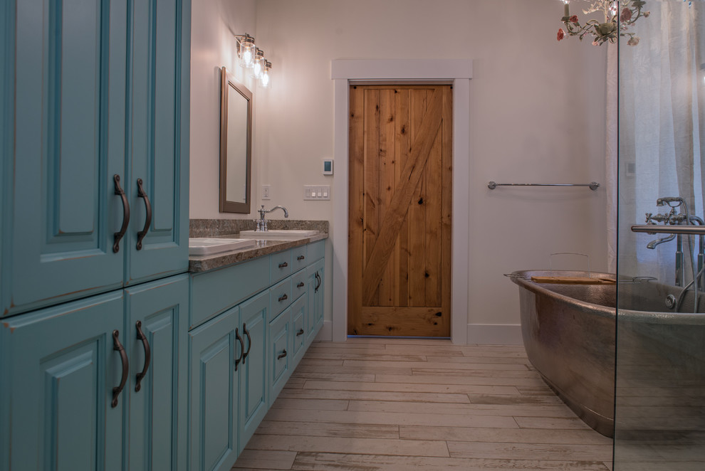 Cette image montre une salle de bain principale rustique avec des portes de placard turquoises, une baignoire indépendante, une douche d'angle, parquet clair, un lavabo intégré, un plan de toilette en marbre, un sol beige, une cabine de douche à porte battante et un plan de toilette gris.