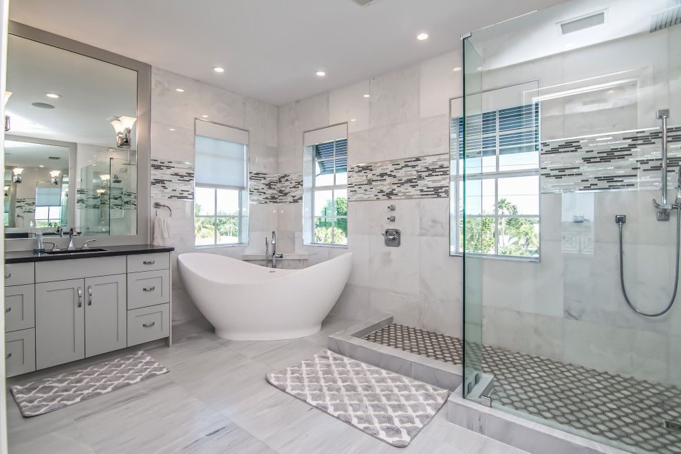 Inspiration for a large beach style ensuite bathroom in Miami with shaker cabinets, grey cabinets, a freestanding bath, a corner shower, grey tiles, porcelain tiles, porcelain flooring, grey floors, an open shower, black worktops, a single sink and a built in vanity unit.