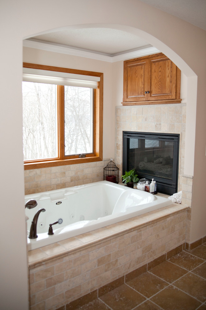 This is an example of a large traditional ensuite bathroom in Minneapolis with a vessel sink, raised-panel cabinets, dark wood cabinets, granite worktops, a built-in bath, a corner shower, a two-piece toilet, brown tiles, stone tiles, beige walls, travertine flooring and brown floors.