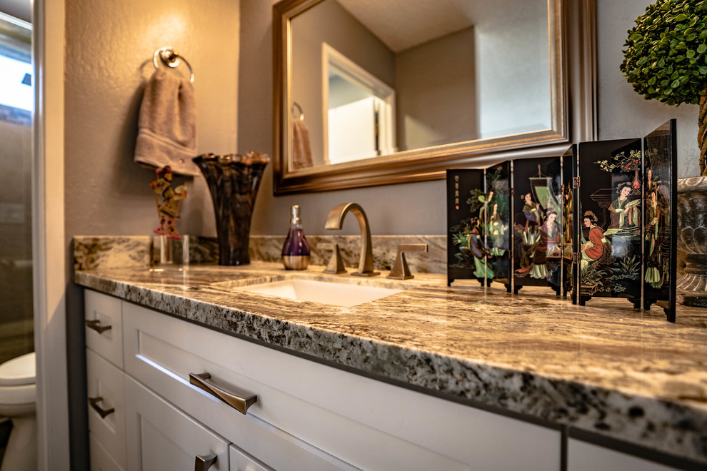 This is an example of a medium sized world-inspired ensuite bathroom in San Francisco with beaded cabinets, white cabinets, a built-in shower, a one-piece toilet, beige tiles, porcelain tiles, grey walls, cement flooring, an integrated sink, granite worktops, black floors, a hinged door and multi-coloured worktops.