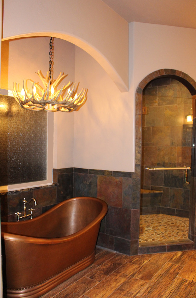 This is an example of a large traditional ensuite bathroom in Oklahoma City with raised-panel cabinets, distressed cabinets, a freestanding bath, a corner shower, a two-piece toilet, multi-coloured tiles, stone tiles, beige walls, ceramic flooring, a submerged sink, granite worktops and a hinged door.