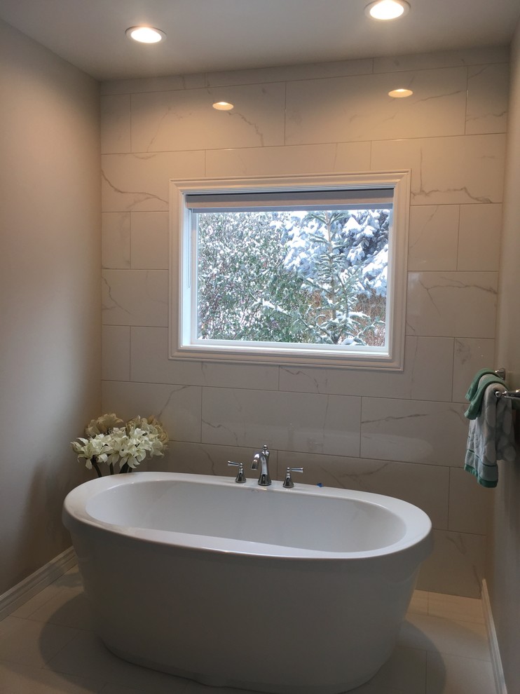 Imagen de cuarto de baño principal actual de tamaño medio con bañera exenta, baldosas y/o azulejos blancos, baldosas y/o azulejos de porcelana, paredes grises, suelo de baldosas de porcelana y suelo blanco
