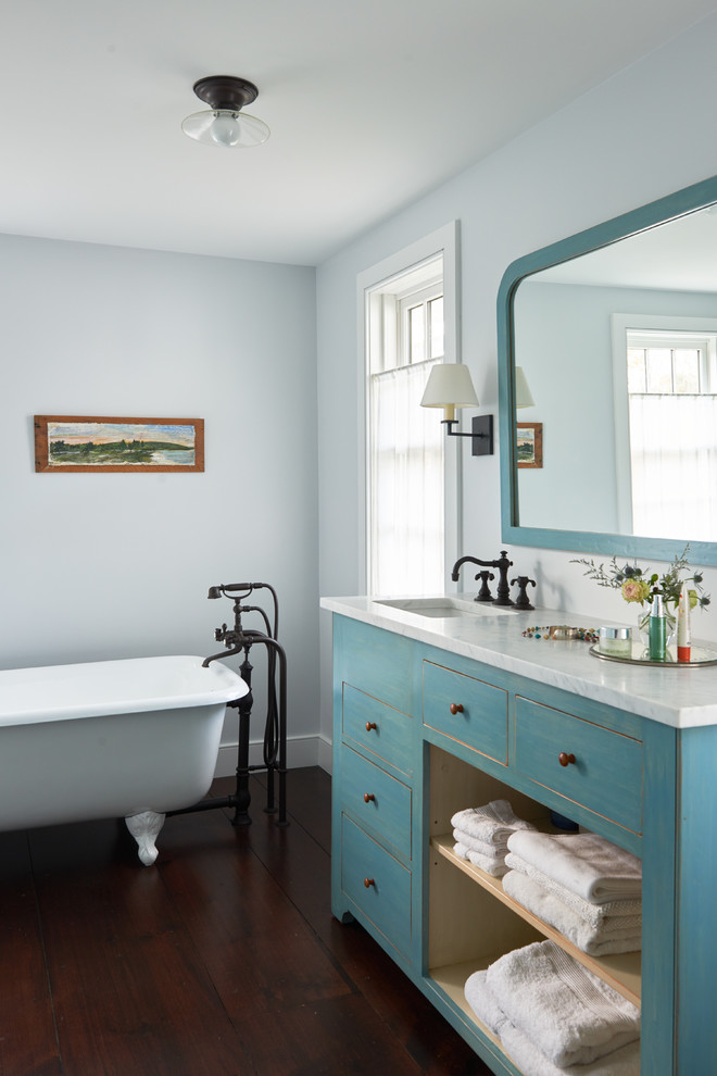 На фото: главная ванная комната среднего размера в стиле кантри с синими фасадами, ванной на ножках, синими стенами, темным паркетным полом, врезной раковиной, мраморной столешницей, коричневым полом и плоскими фасадами
