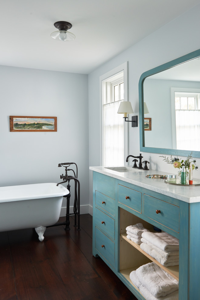 Mid-sized farmhouse master dark wood floor and brown floor claw-foot bathtub photo in New York with blue cabinets, blue walls, an undermount sink, marble countertops and furniture-like cabinets
