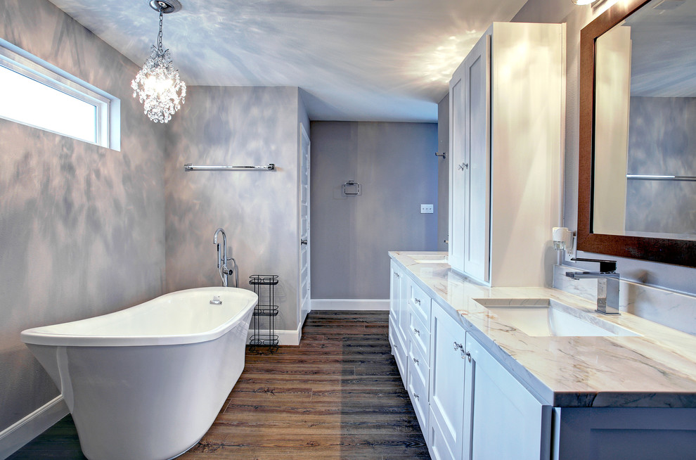 Bild på ett stort funkis en-suite badrum, med skåp i shakerstil, vita skåp, ett fristående badkar, en toalettstol med hel cisternkåpa, grå väggar, mörkt trägolv, ett undermonterad handfat, marmorbänkskiva och brunt golv