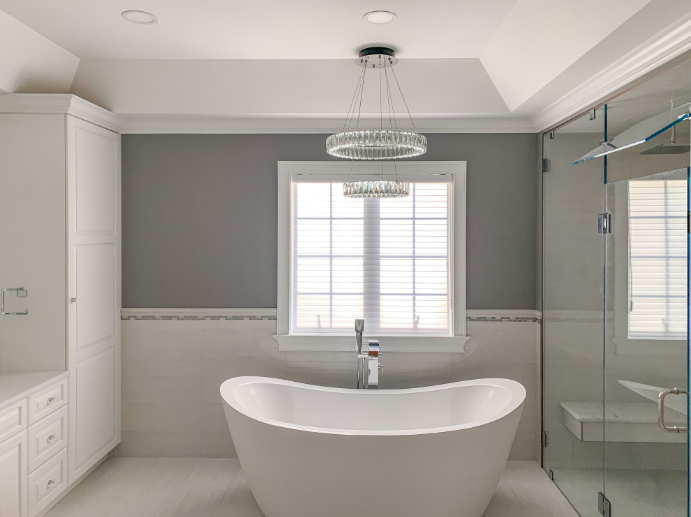Expansive classic ensuite bathroom with raised-panel cabinets, white cabinets, a freestanding bath, a built-in shower, a one-piece toilet, white tiles, porcelain tiles, grey walls, porcelain flooring, a vessel sink, engineered stone worktops, white floors, a hinged door and white worktops.