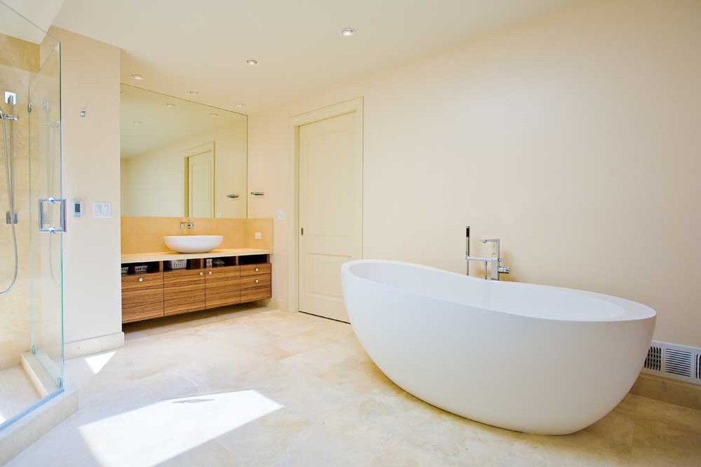 This is an example of a modern bathroom in San Francisco with a vessel sink, flat-panel cabinets, medium wood cabinets, limestone worktops, a freestanding bath, a corner shower, a one-piece toilet, beige tiles, stone tiles, beige walls and limestone flooring.