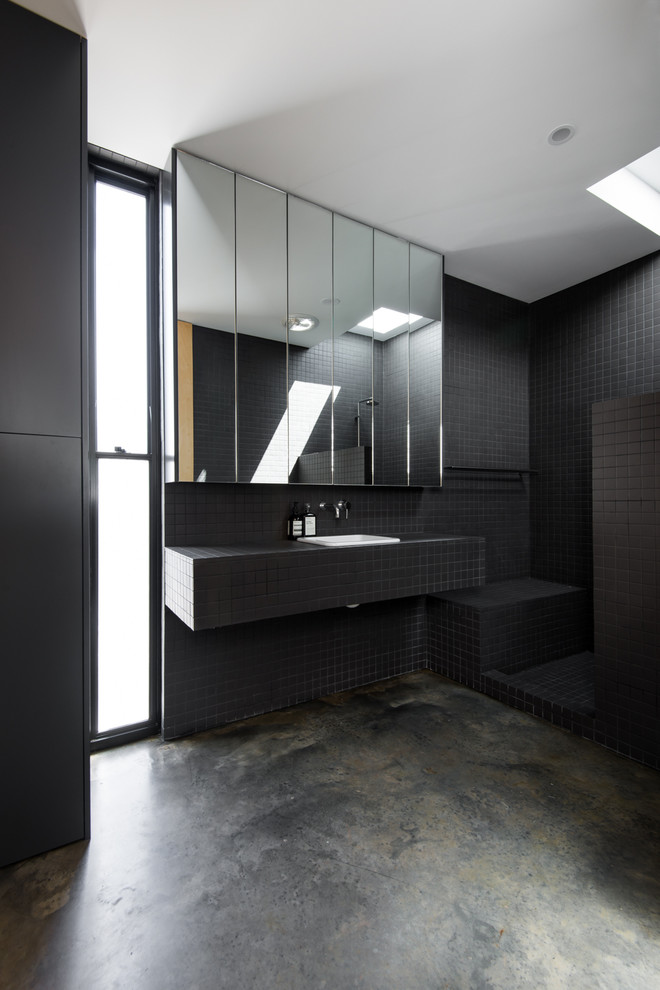 Inspiration för små moderna en-suite badrum, med ett integrerad handfat, svarta skåp, kaklad bänkskiva, en öppen dusch, en toalettstol med hel cisternkåpa, svart kakel, keramikplattor, svarta väggar och betonggolv