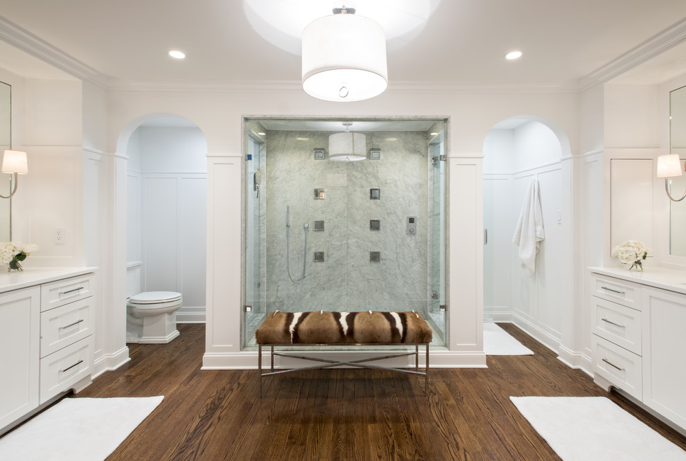 Inspiration for a large timeless master stone slab medium tone wood floor double shower remodel in Louisville with an undermount sink, raised-panel cabinets, white cabinets, solid surface countertops, a two-piece toilet and white walls
