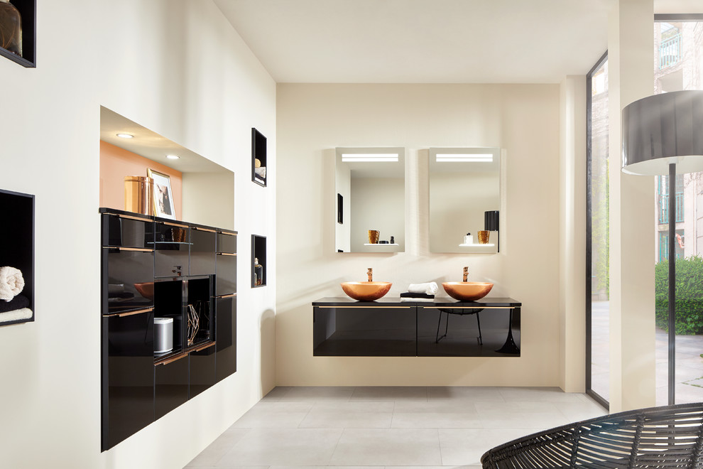 Cette photo montre une salle de bain moderne avec un placard à porte plane, des portes de placard noires, un mur blanc, une vasque, un sol beige et un plan de toilette noir.