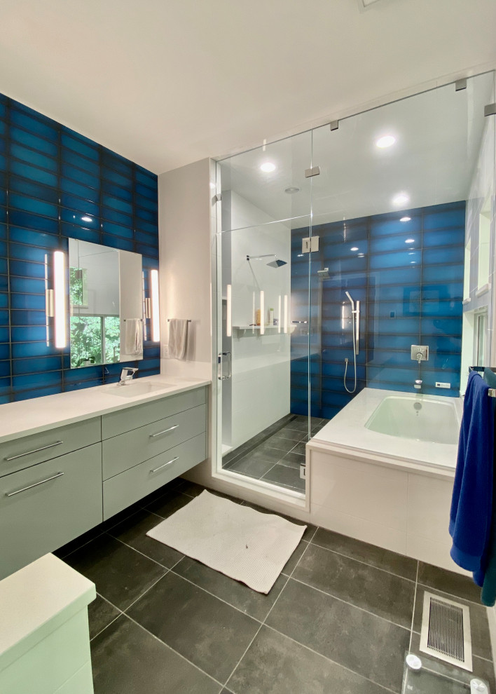 Источник вдохновения для домашнего уюта: главная ванная комната среднего размера в современном стиле с плоскими фасадами, серыми фасадами, полновстраиваемой ванной, душем над ванной, унитазом-моноблоком, синей плиткой, стеклянной плиткой, белыми стенами, полом из керамической плитки, врезной раковиной, столешницей из искусственного кварца, серым полом, душем с распашными дверями, белой столешницей, нишей, тумбой под две раковины и подвесной тумбой