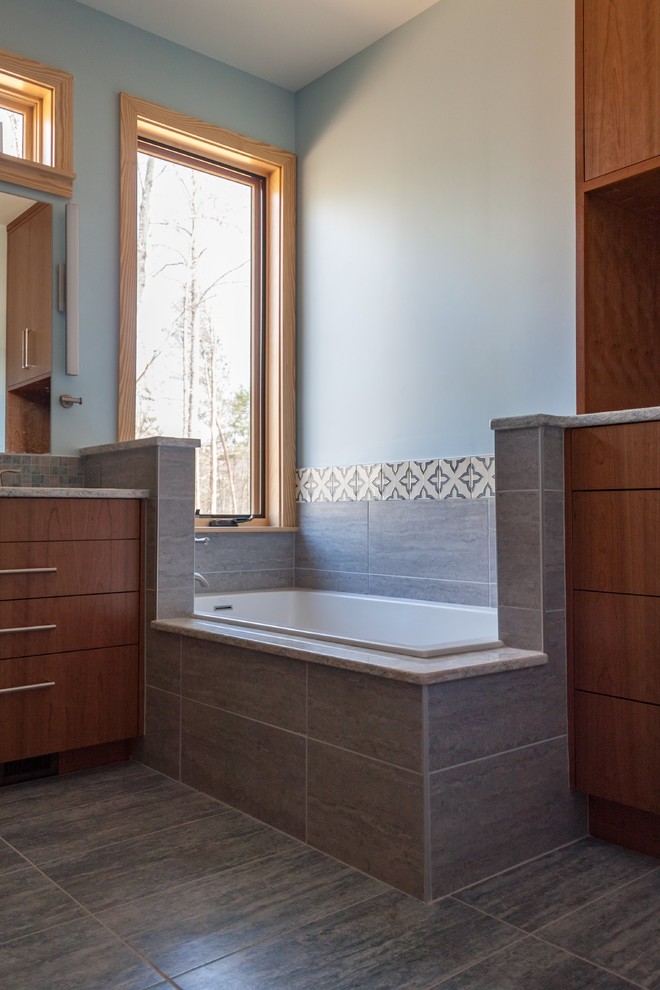 Photo of a medium sized contemporary ensuite bathroom in Raleigh with flat-panel cabinets, medium wood cabinets, a built-in bath, an alcove shower, a one-piece toilet, blue tiles, ceramic tiles, blue walls, ceramic flooring, a submerged sink, engineered stone worktops, grey floors, a hinged door and multi-coloured worktops.