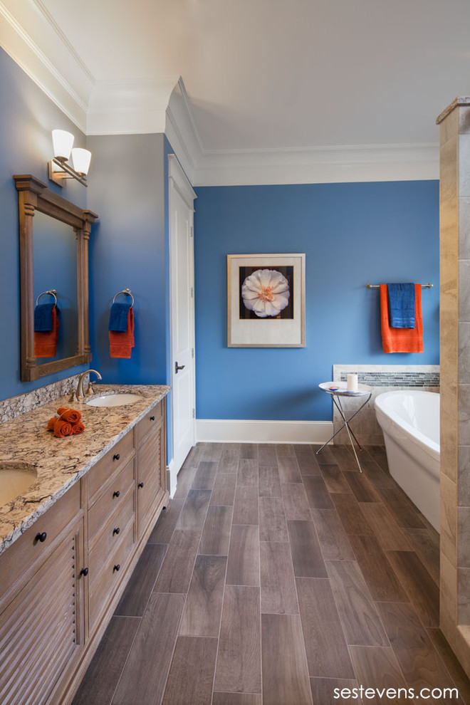 Foto de cuarto de baño principal tradicional con lavabo bajoencimera, armarios con paneles lisos, puertas de armario de madera clara, bañera exenta, paredes azules y suelo de madera en tonos medios