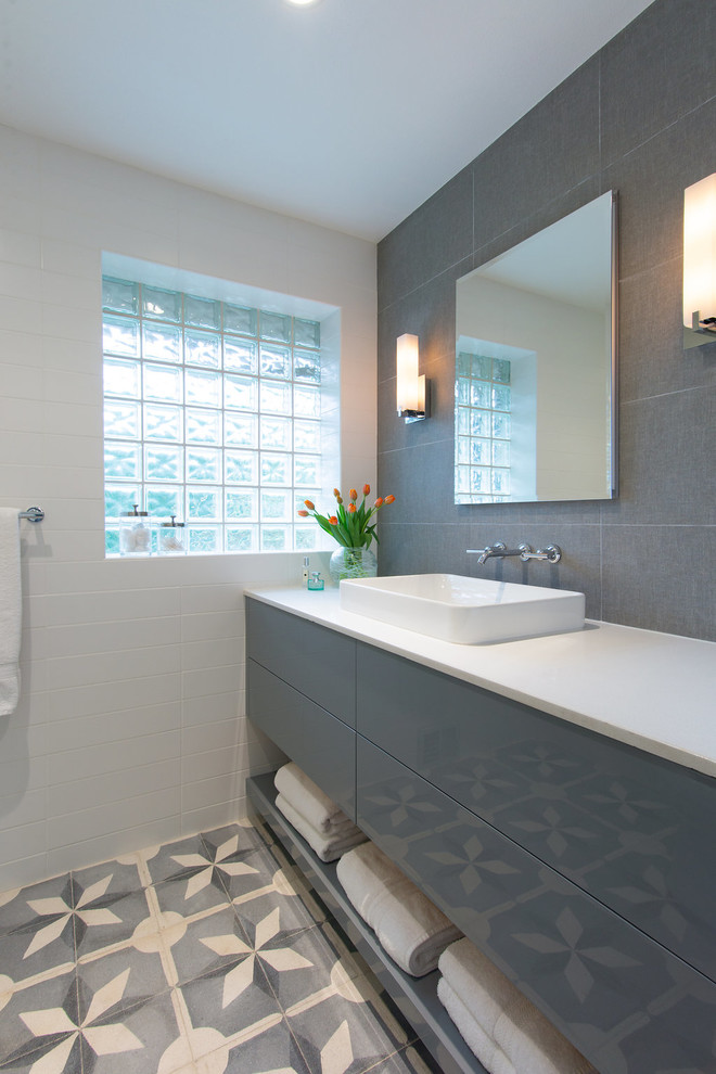 Modern inredning av ett en-suite badrum, med släta luckor, grå skåp, en dusch i en alkov, en toalettstol med separat cisternkåpa, vit kakel, tunnelbanekakel, vita väggar, cementgolv, ett fristående handfat, bänkskiva i akrylsten, grått golv och dusch med gångjärnsdörr