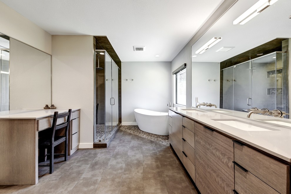 Inspiration for a large modern ensuite bathroom in Austin with flat-panel cabinets, light wood cabinets, a freestanding bath, a walk-in shower, a one-piece toilet, grey tiles, ceramic tiles, grey walls, ceramic flooring, a submerged sink, engineered stone worktops, grey floors and a hinged door.