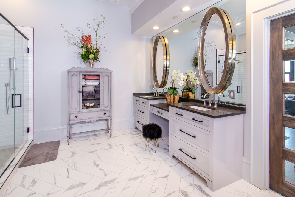 Photo of a large urban bathroom in Charlotte with grey cabinets, a freestanding bath, a corner shower, grey tiles, metro tiles, grey walls, marble flooring, a vessel sink, white floors and a hinged door.