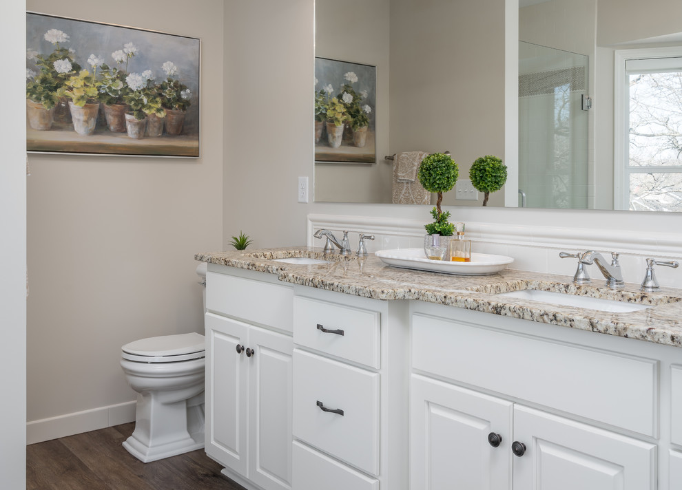 Inspiration for a mid-sized transitional master beige tile and ceramic tile vinyl floor and brown floor bathroom remodel in Minneapolis with raised-panel cabinets, white cabinets, a two-piece toilet, beige walls, an undermount sink, granite countertops, a hinged shower door and beige countertops