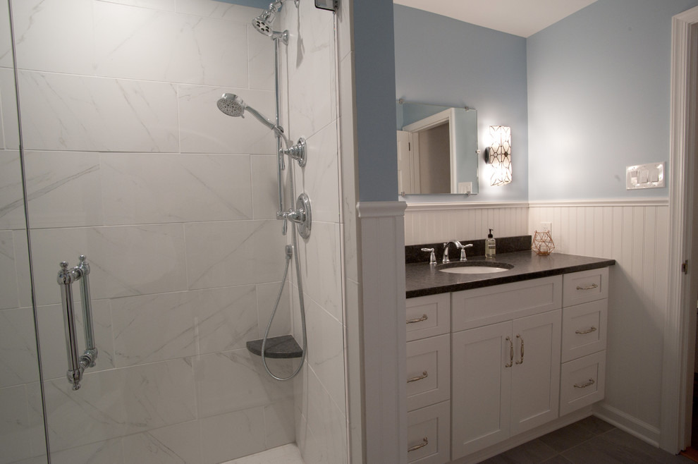 This is an example of a medium sized traditional ensuite bathroom in Philadelphia with white cabinets, an alcove shower, a two-piece toilet, white tiles, ceramic tiles, blue walls, cement flooring, a submerged sink, grey floors, a hinged door, shaker cabinets, solid surface worktops and black worktops.