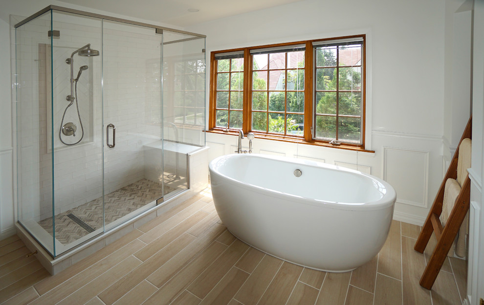 This is an example of a large classic ensuite bathroom in New York with recessed-panel cabinets, brown cabinets, a freestanding bath, a two-piece toilet, white tiles, ceramic tiles, white walls, ceramic flooring, a submerged sink, engineered stone worktops, beige floors, a hinged door and white worktops.