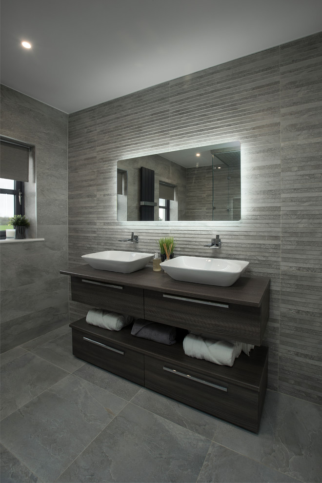 Стильный дизайн: большая главная ванная комната в современном стиле с душем без бортиков, унитазом-моноблоком, серой плиткой, серыми стенами, подвесной раковиной, серым полом, душем с распашными дверями и серой столешницей - последний тренд