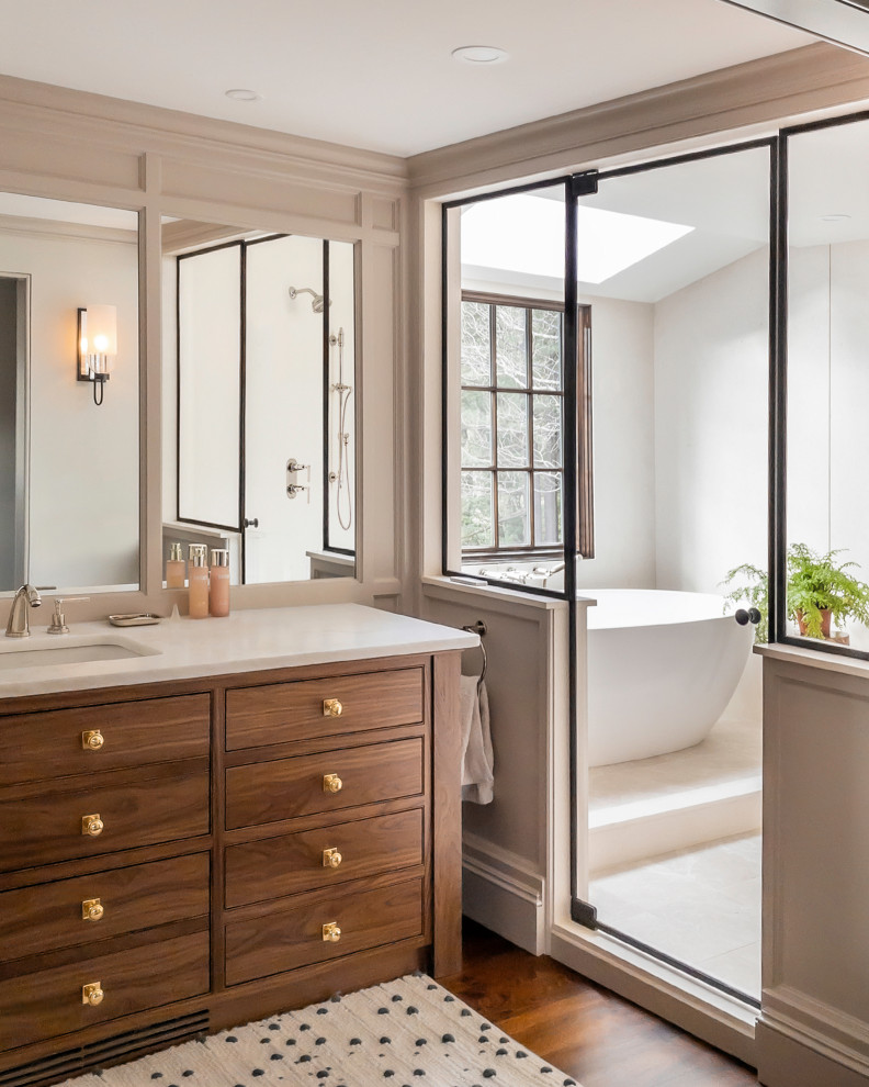 Traditional wet room bathroom in Boston with beaded cabinets, medium wood cabinets, a freestanding bath, grey walls, dark hardwood flooring, a submerged sink, brown floors, white worktops, a built in vanity unit, double sinks, beige tiles and stone slabs.