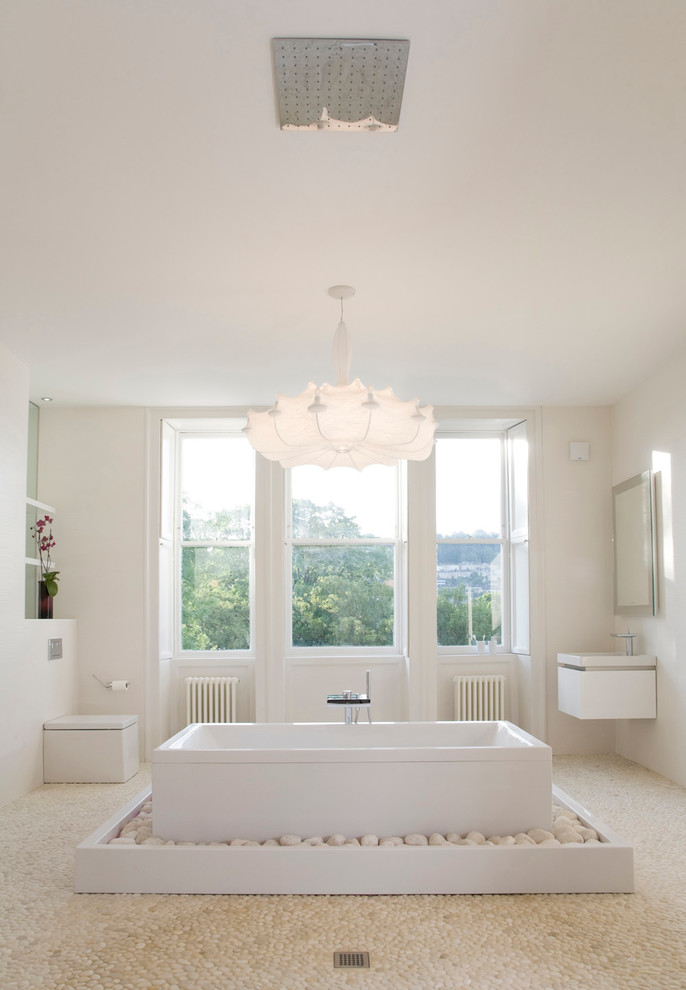 Стильный дизайн: большая главная ванная комната в стиле модернизм с подвесной раковиной, отдельно стоящей ванной, открытым душем, унитазом-моноблоком, белой плиткой, керамической плиткой, белыми стенами и полом из галечной плитки - последний тренд