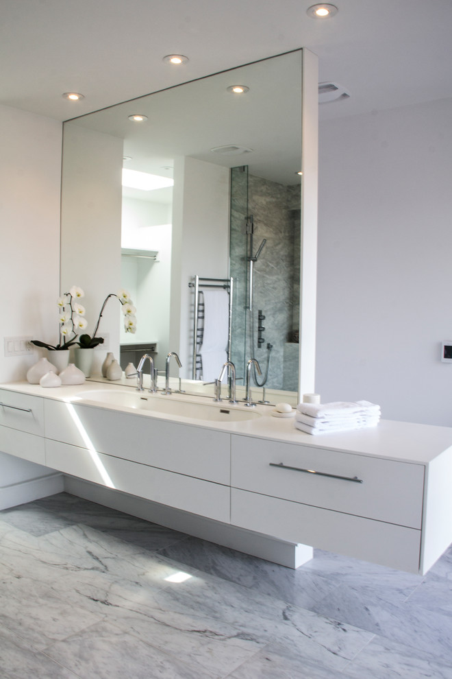 Источник вдохновения для домашнего уюта: главная ванная комната в стиле модернизм с плоскими фасадами, белыми фасадами, отдельно стоящей ванной, унитазом-моноблоком, белой плиткой, мраморной плиткой, белыми стенами, мраморным полом, раковиной с несколькими смесителями, столешницей из искусственного камня, белым полом и душем с распашными дверями