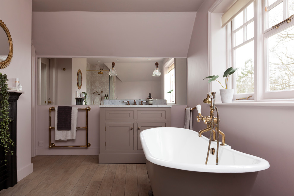 Foto de cuarto de baño tradicional con armarios estilo shaker, puertas de armario violetas, bañera con patas, paredes púrpuras, suelo de madera en tonos medios, suelo marrón y encimeras blancas