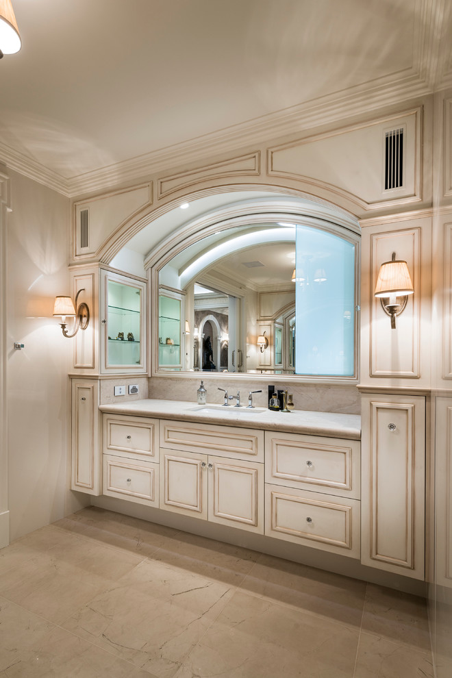 Exemple d'une grande salle de bain principale chic en bois vieilli avec un placard avec porte à panneau encastré, une douche double, un carrelage beige, un carrelage de pierre, un mur beige, un sol en marbre, un lavabo encastré et un plan de toilette en marbre.