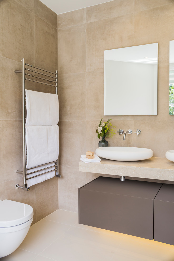 Inspiration for a medium sized contemporary ensuite bathroom in London with flat-panel cabinets, grey cabinets, a freestanding bath, a walk-in shower, a wall mounted toilet, beige tiles, ceramic tiles, beige walls, ceramic flooring, a vessel sink, engineered stone worktops, white floors, a sliding door and beige worktops.
