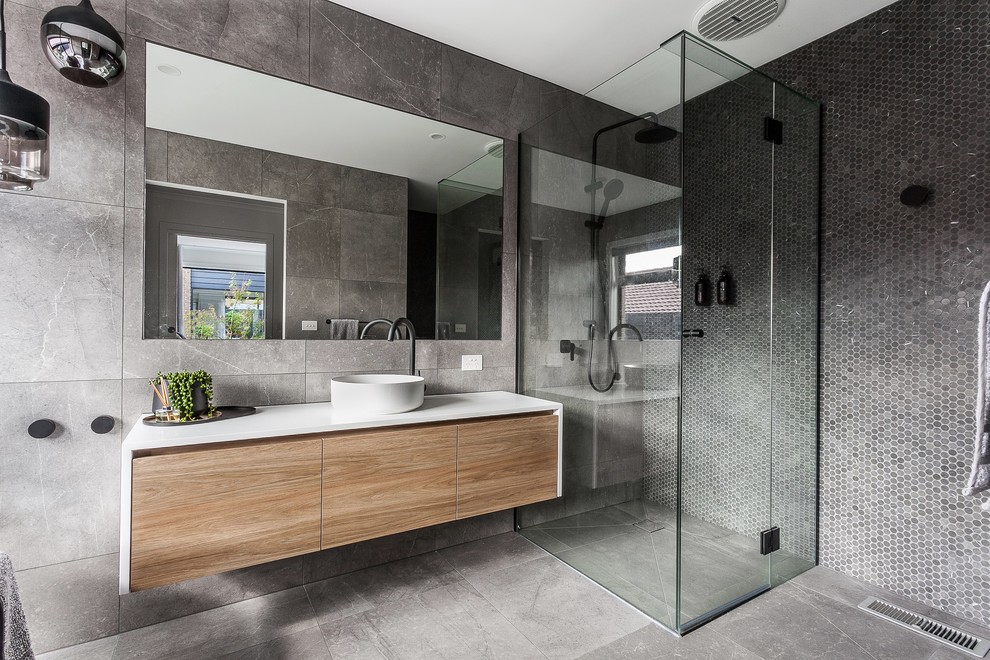 Inspiration for a mid-sized modern master gray tile gray floor bathroom remodel in Melbourne with open cabinets, medium tone wood cabinets, a two-piece toilet, gray walls, a drop-in sink, quartz countertops, a hinged shower door and white countertops