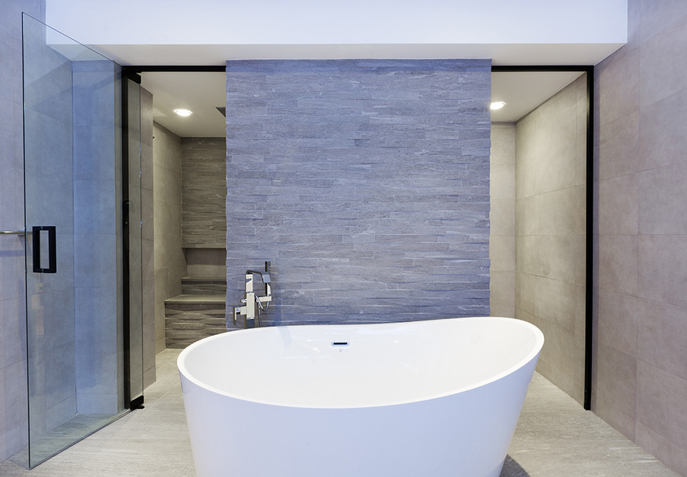 This is an example of a large modern ensuite wet room bathroom in New York with flat-panel cabinets, light wood cabinets, a freestanding bath, a one-piece toilet, grey tiles, porcelain tiles, grey walls, porcelain flooring, a submerged sink, engineered stone worktops, grey floors and a hinged door.