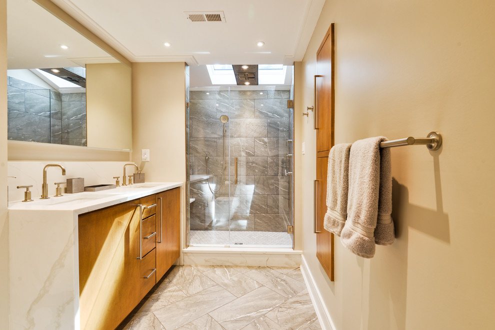 Trendy 3/4 gray tile beige floor alcove shower photo in Philadelphia with flat-panel cabinets, medium tone wood cabinets, beige walls, an undermount sink, a hinged shower door and white countertops