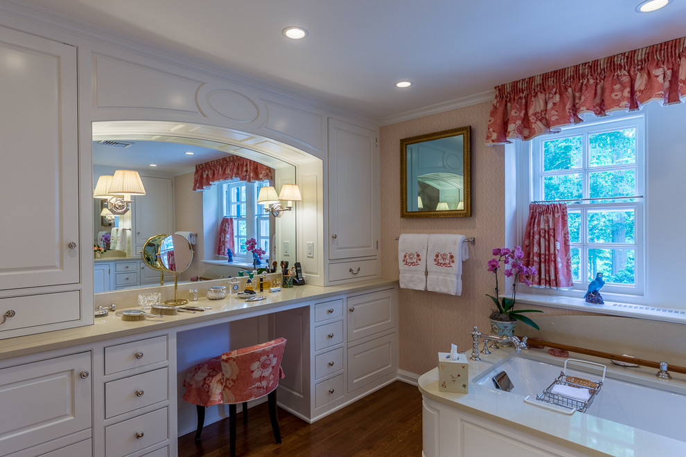 Modelo de cuarto de baño principal clásico grande con lavabo integrado, armarios con paneles con relieve, puertas de armario blancas, jacuzzi, paredes rosas y suelo de madera en tonos medios