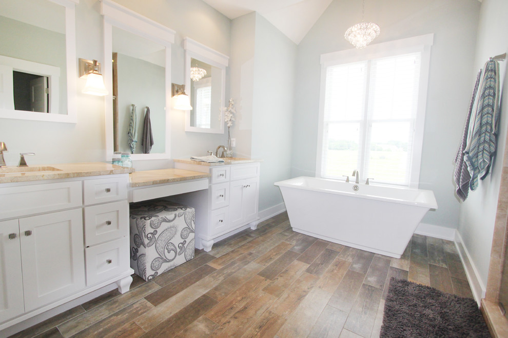 Modelo de cuarto de baño principal clásico con puertas de armario blancas, encimera de mármol, bañera exenta y suelo de madera en tonos medios