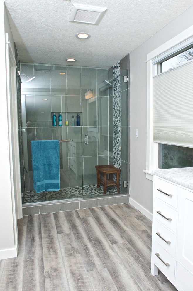На фото: ванная комната среднего размера с фасадами с утопленной филенкой, белыми фасадами, двойным душем, серой плиткой, серыми стенами, полом из ламината, душевой кабиной, врезной раковиной и мраморной столешницей с