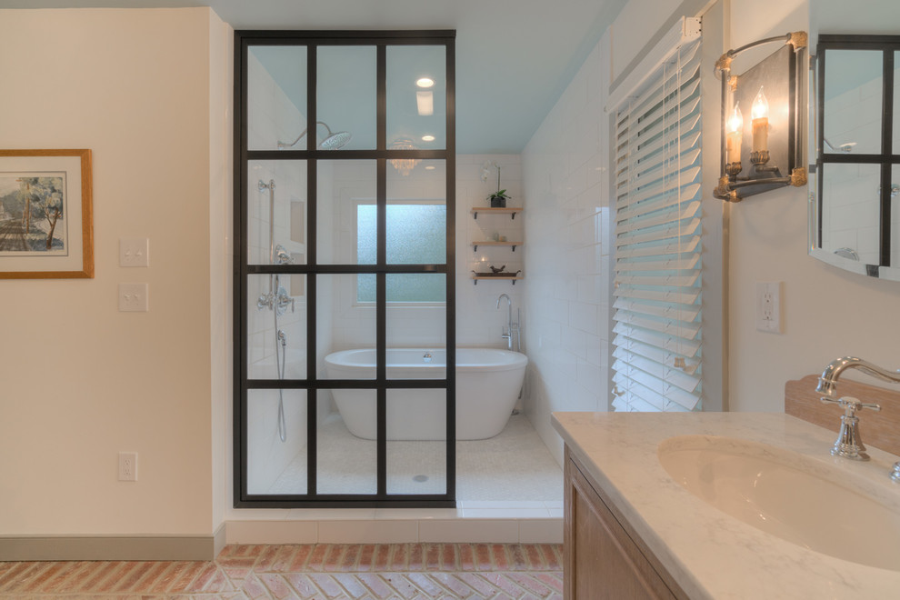 This is an example of a medium sized traditional ensuite bathroom in DC Metro with recessed-panel cabinets, light wood cabinets, a freestanding bath, a shower/bath combination, a one-piece toilet, white walls, brick flooring and a submerged sink.