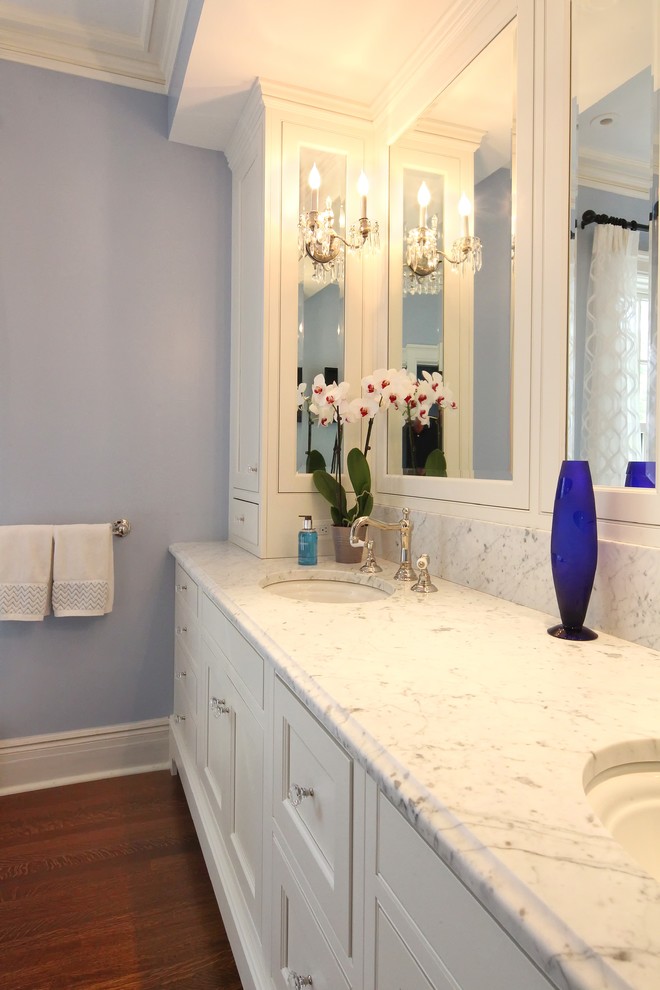 Klassisk inredning av ett vit vitt badrum, med luckor med profilerade fronter, vita skåp, ett fristående badkar, en dusch i en alkov, vit kakel, marmorkakel, lila väggar, ett undermonterad handfat, marmorbänkskiva och med dusch som är öppen