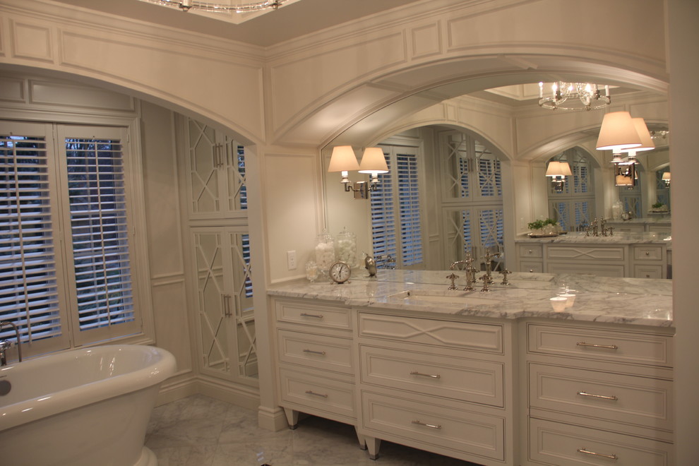 Foto de cuarto de baño principal tradicional con puertas de armario blancas, bañera exenta, paredes blancas, suelo de mármol, lavabo bajoencimera y encimera de mármol