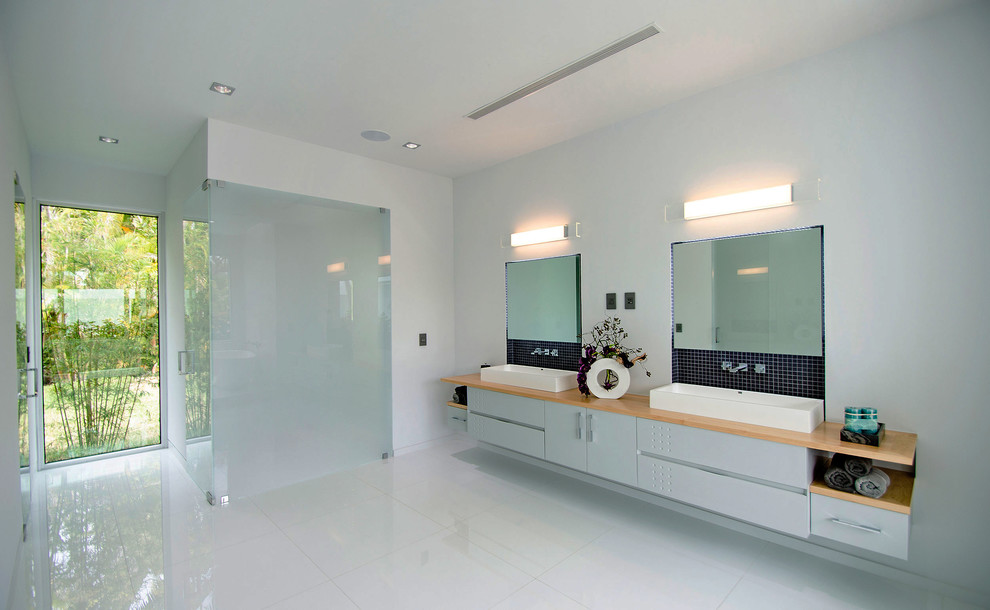 Photo of a medium sized modern ensuite bathroom in Miami with freestanding cabinets, grey cabinets, a walk-in shower, a one-piece toilet, grey tiles, stone slabs, white walls, porcelain flooring, wooden worktops and a vessel sink.