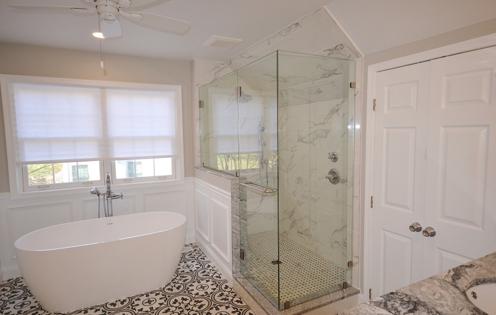 Photo of a large classic ensuite bathroom in Philadelphia with raised-panel cabinets, white cabinets, a freestanding bath, a corner shower, a one-piece toilet, black and white tiles, marble tiles, grey walls, ceramic flooring, a submerged sink, granite worktops, multi-coloured floors, a hinged door, multi-coloured worktops, a shower bench, double sinks, a built in vanity unit, a vaulted ceiling and wainscoting.